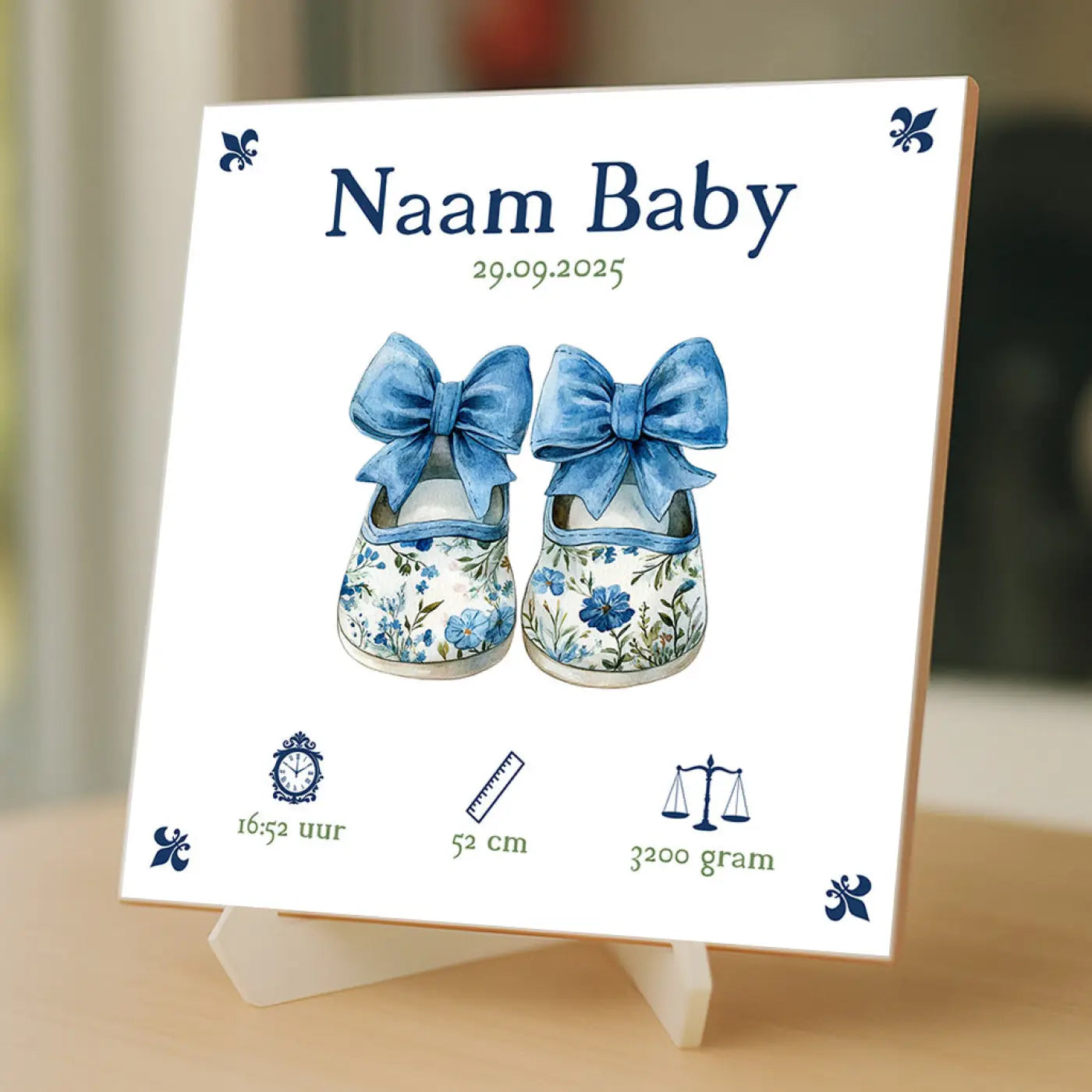 Een wit baby tegeltje met blauwe aquarel babyschoentjes met grote strikken en marineblauwe fleur de lis motieven
