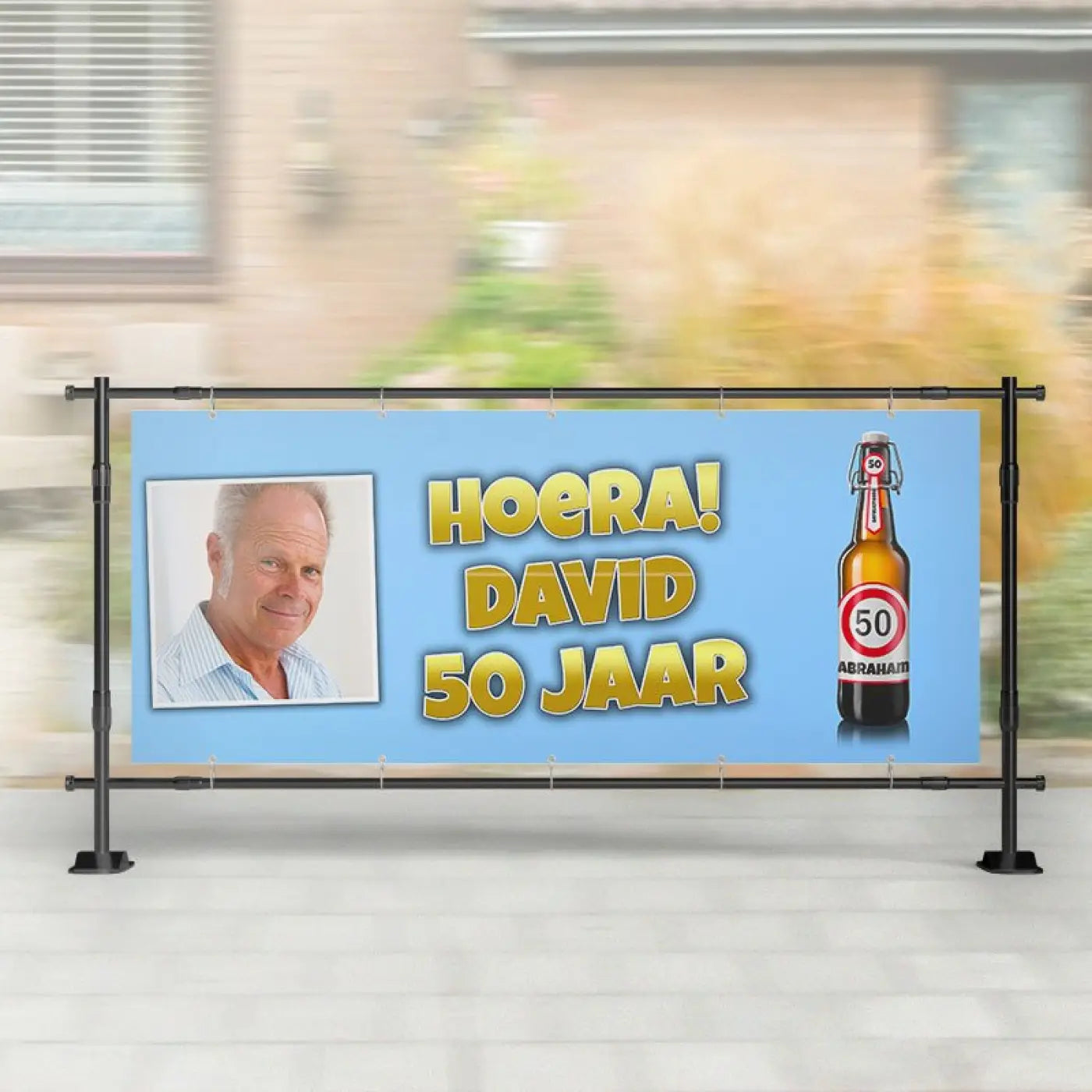 Lichtblauw spandoek abraham met gele tekst hoera david 50 jaar en foto van oudere man met bierviltje rechterzijde