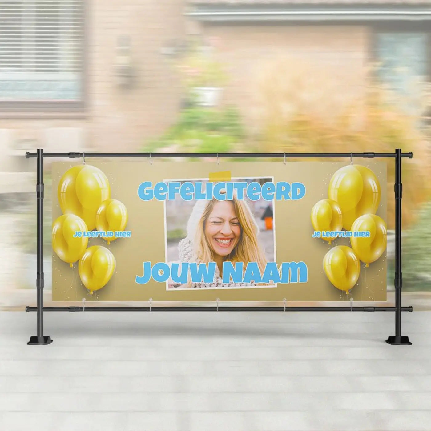 A beige spandoek verjaardag met blauwe tekst gele ballonnen en foto van een lachende vrouw centraal geplaatst